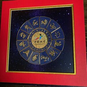 China winter sports zodiac pins mounted in a red and gold matting in a 10" frame